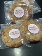 12 Goji White Chocolate Lactation Cookies. Three cookies in clear packaging with 'Boobin Delicious' labels on a dark surface.