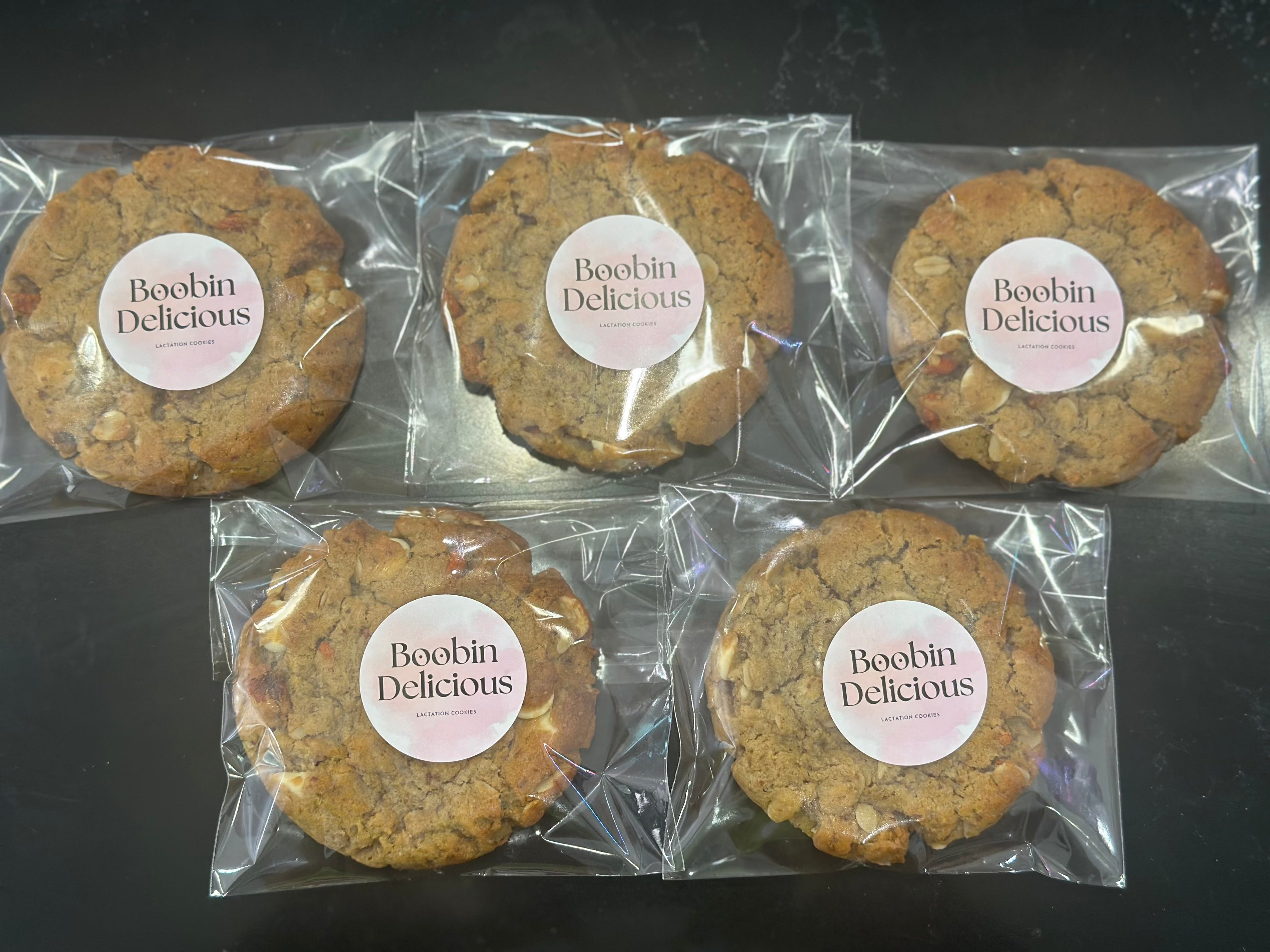 12 Goji White Chocolate Lactation Cookies. Five cookies in clear packaging with 'Boobin delicious' labels on a dark background